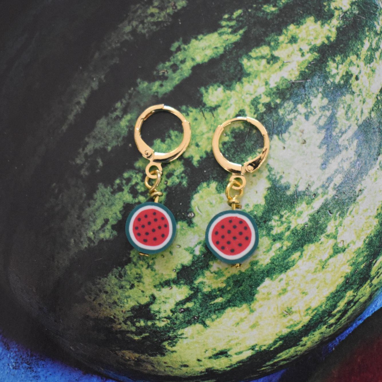 Gold hoop earrings with watermelon slice charms on a watermelon background