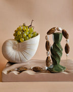Decorative piece with a shell, grapes, and a green sculpture on a beige background