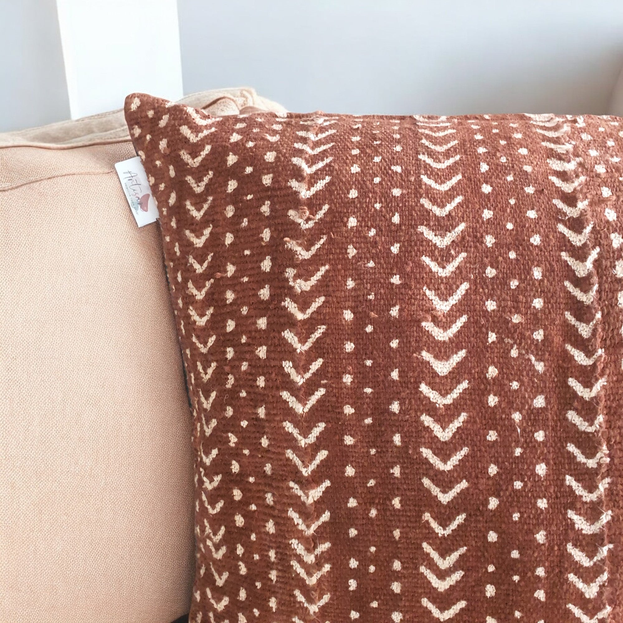 Patterned brown pillow on a beige couch with a white wall background