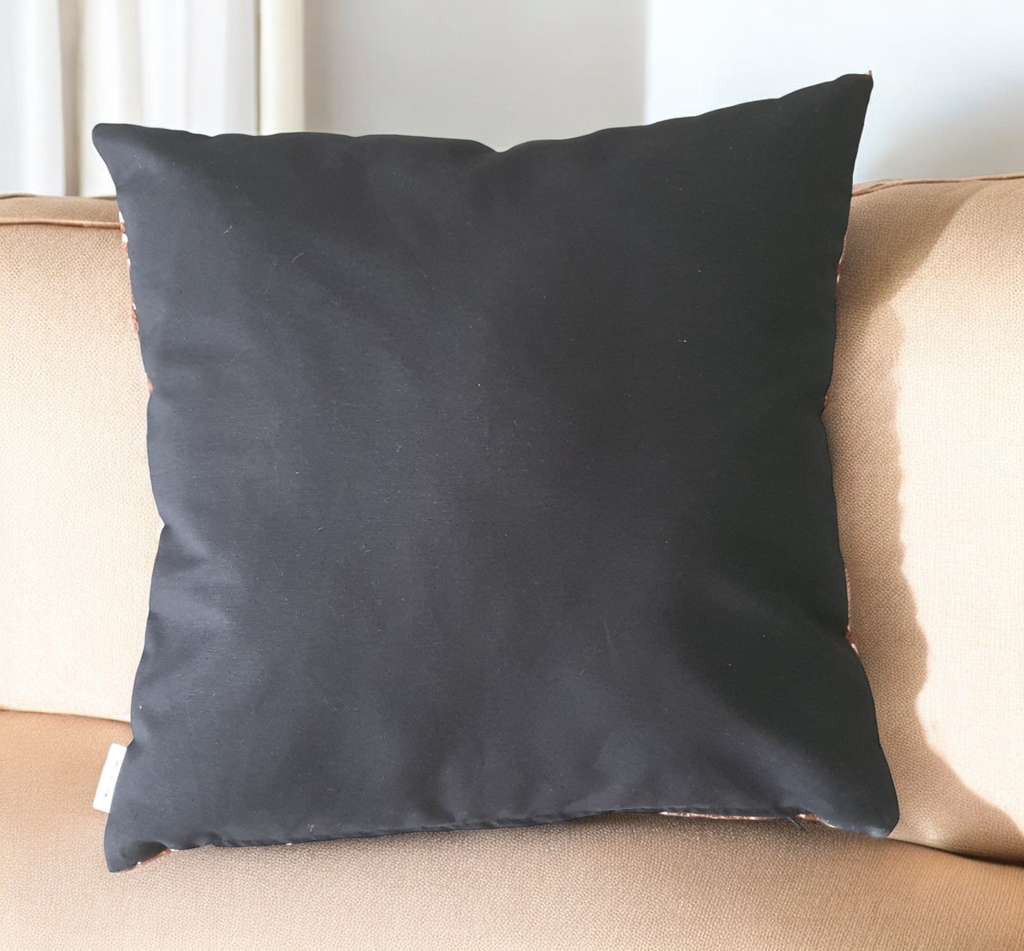 Black pillow on a beige couch with a neutral background