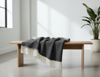 Wooden bench with a dark gray blanket draped over it in a minimalistic room with a plant.
