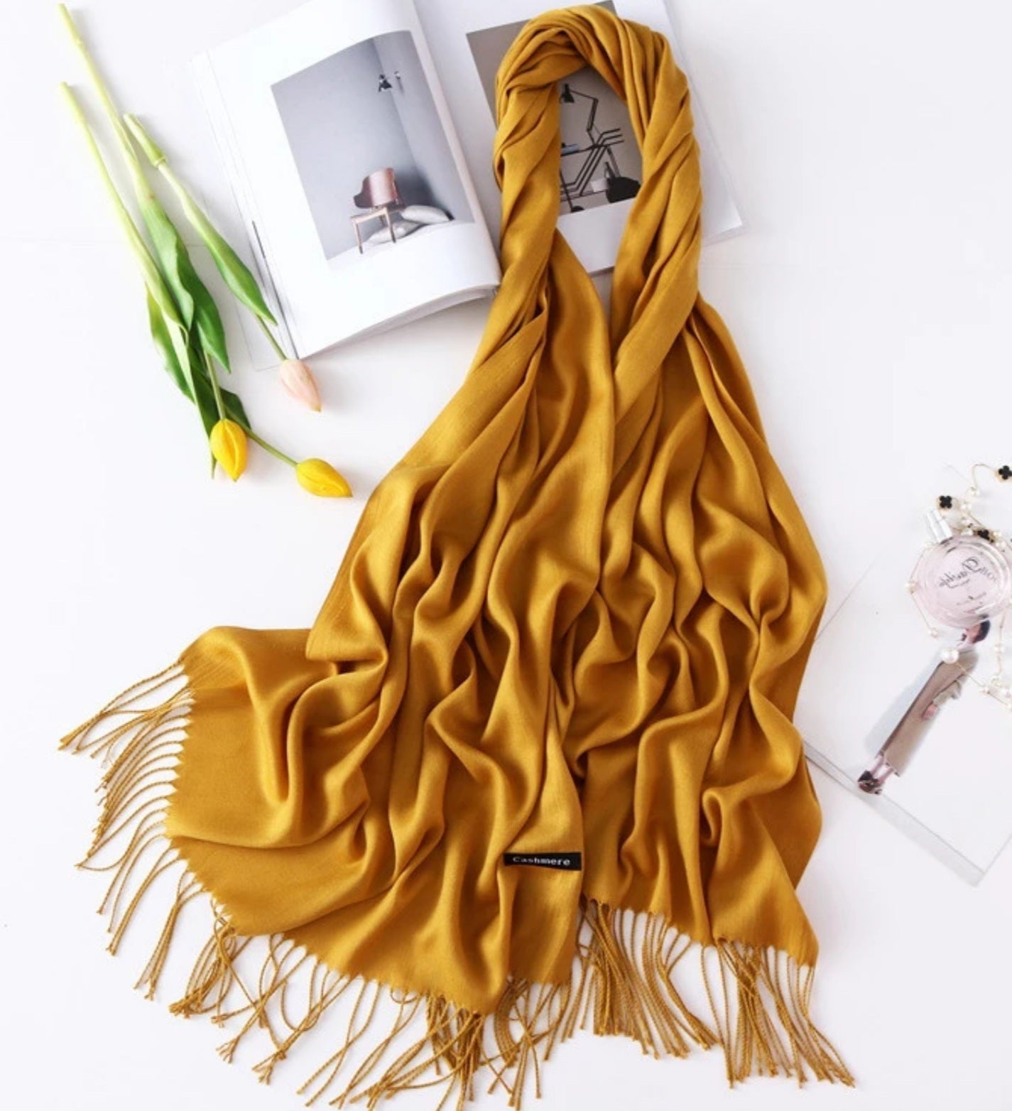 Yellow scarf with fringes on a white surface with a magazine and tulips.