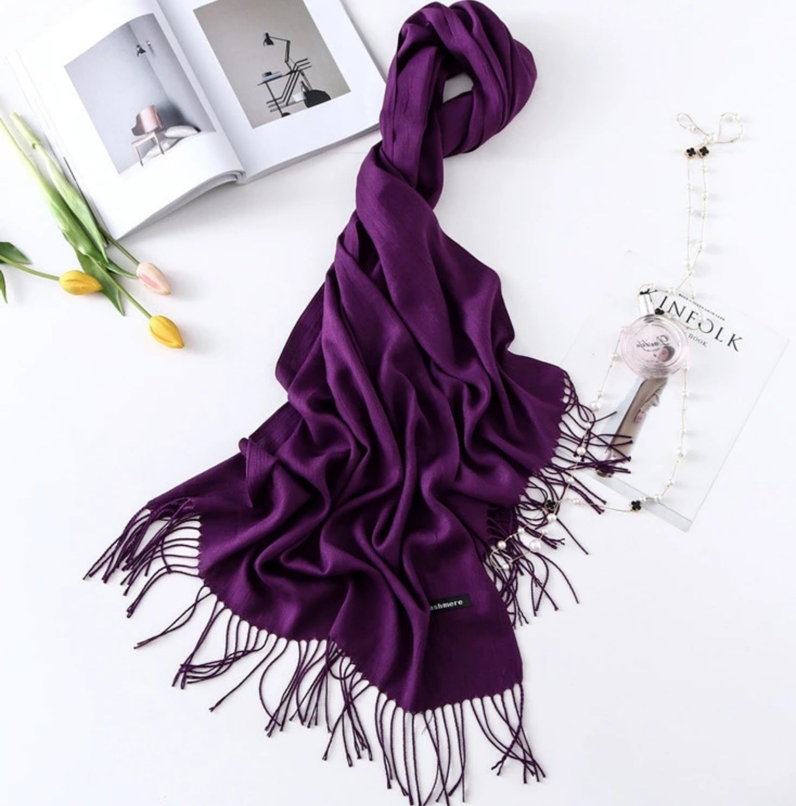 Purple scarf with tassels on a white surface with a book and tulips.