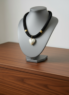 Black choker necklace with gold accents and a heart-shaped pearl pendant on a light gray stand on a dresser