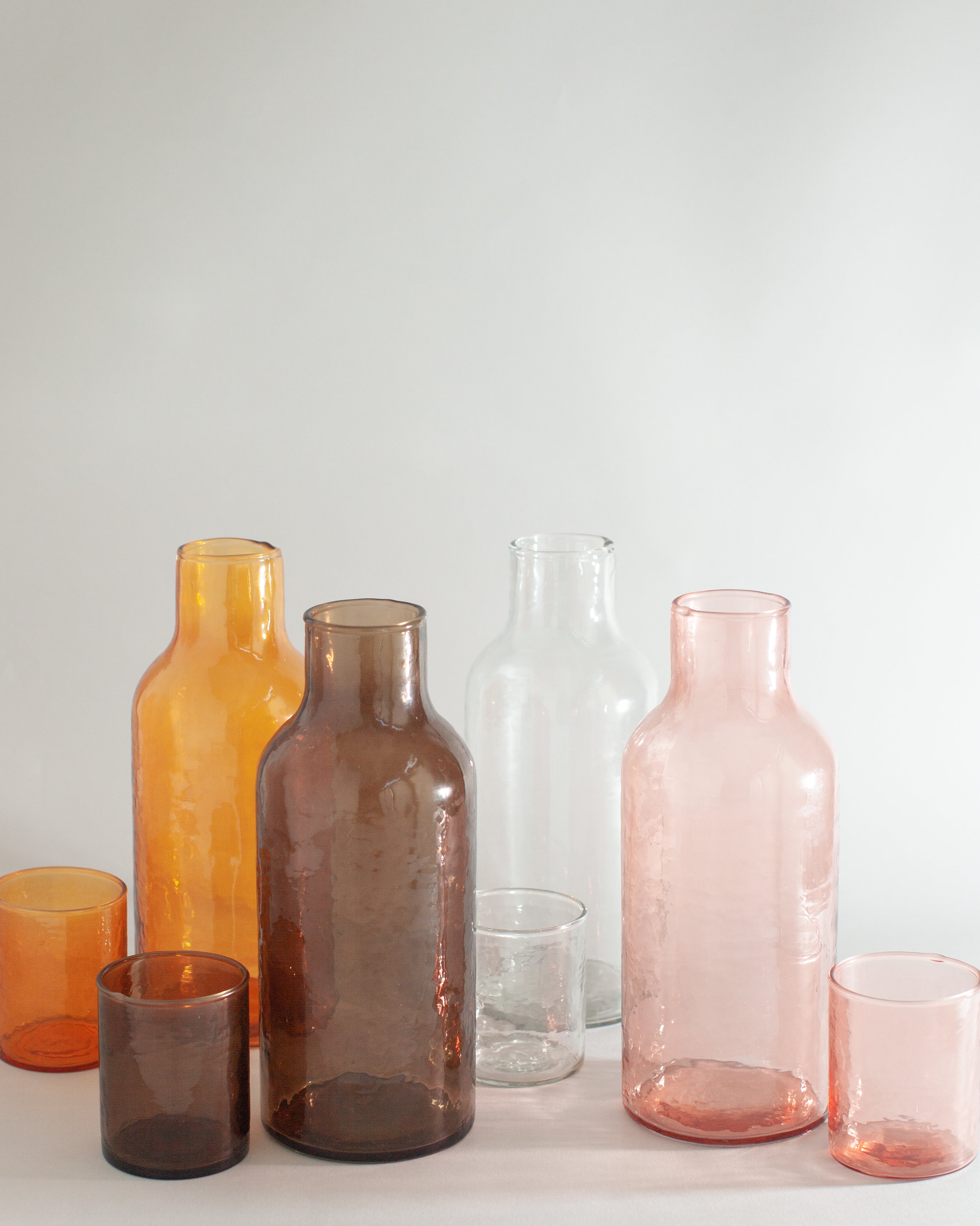 Set of colorful glass bottles and tumblers on a light surface with a neutral background