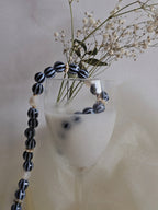 Black and white beaded necklace draped over a glass with flowers on a neutral background