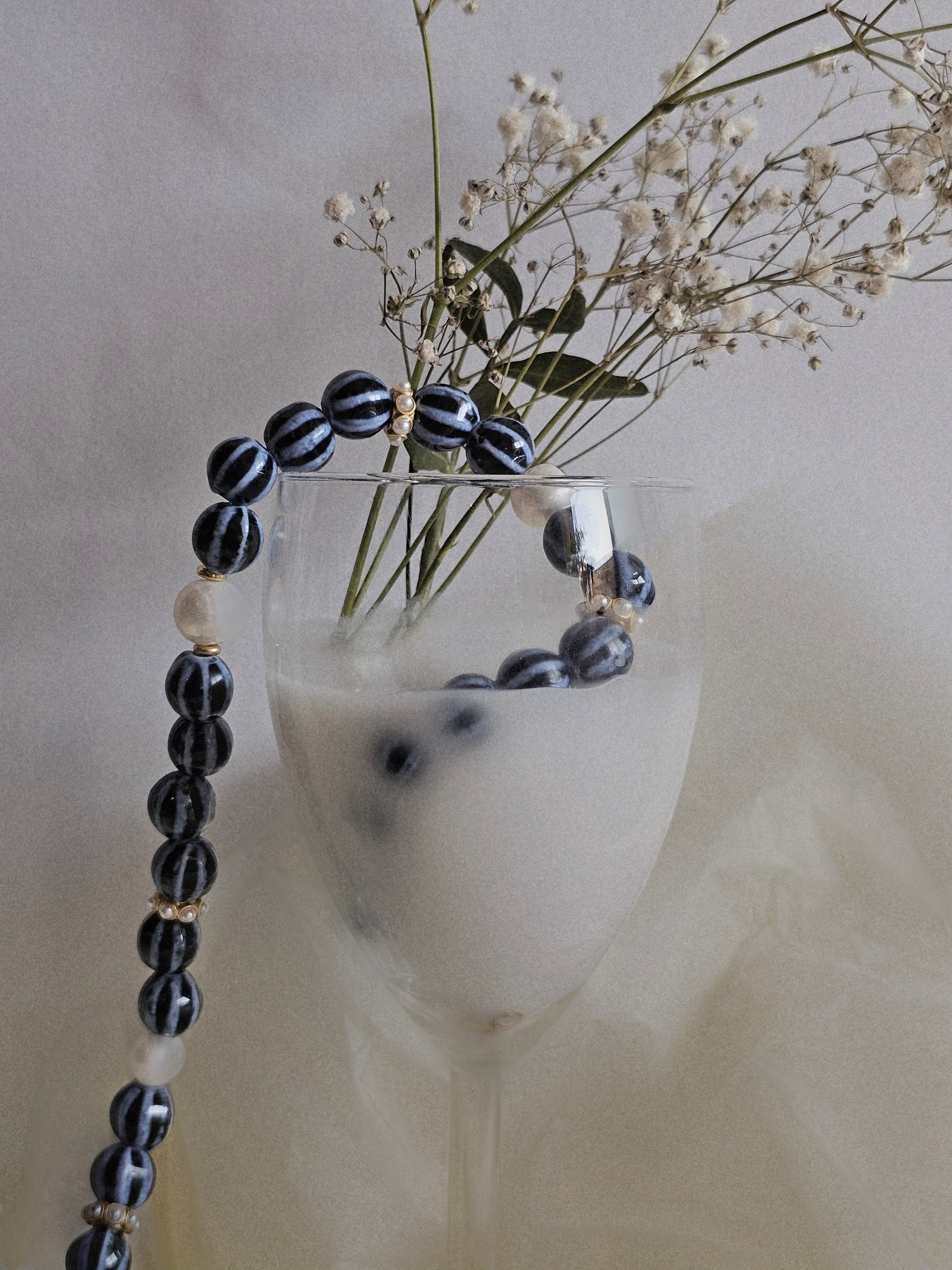 Black and white beaded necklace draped over a glass with flowers on a neutral background