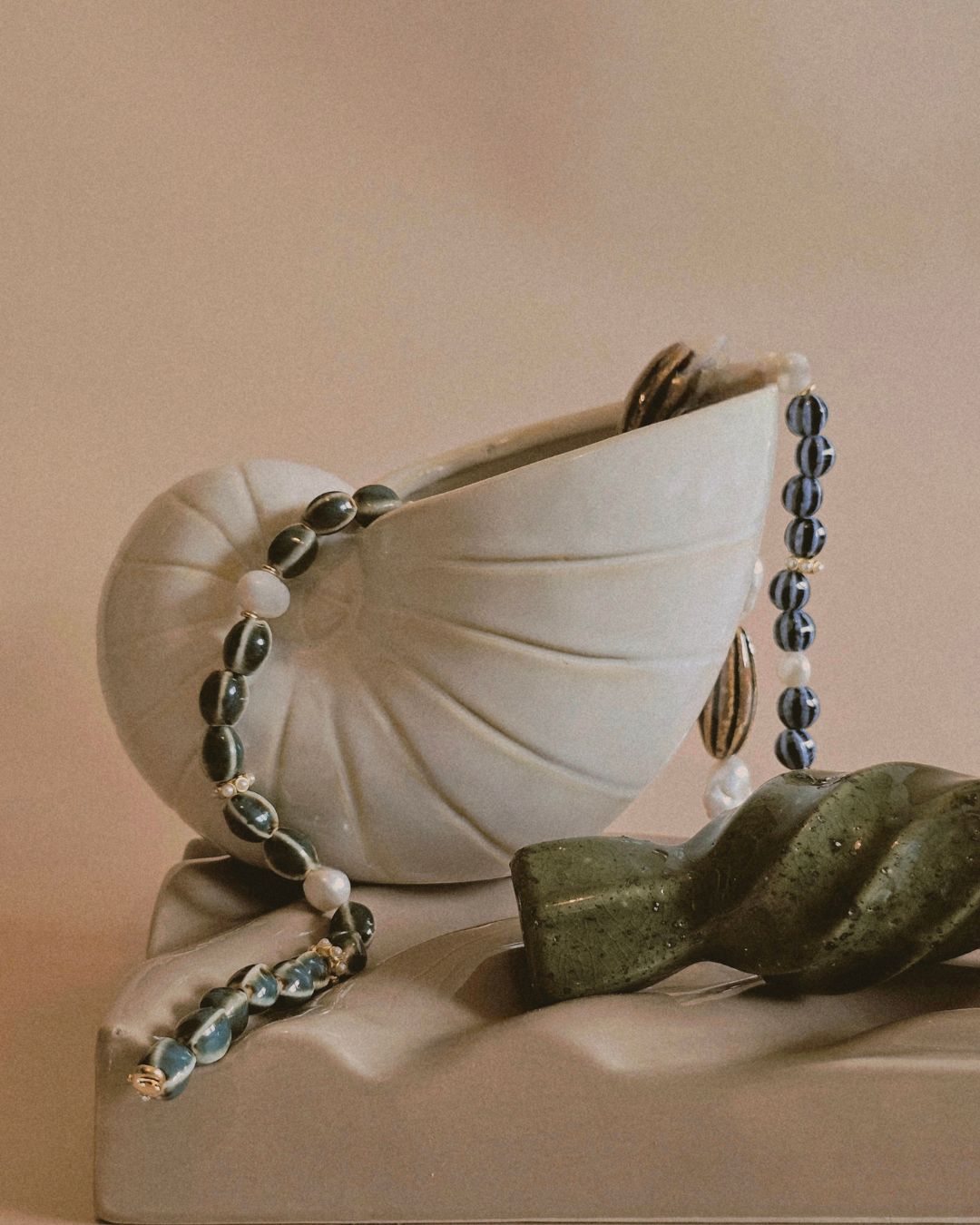 Ceramic shell with a necklace draped over it on a beige background
