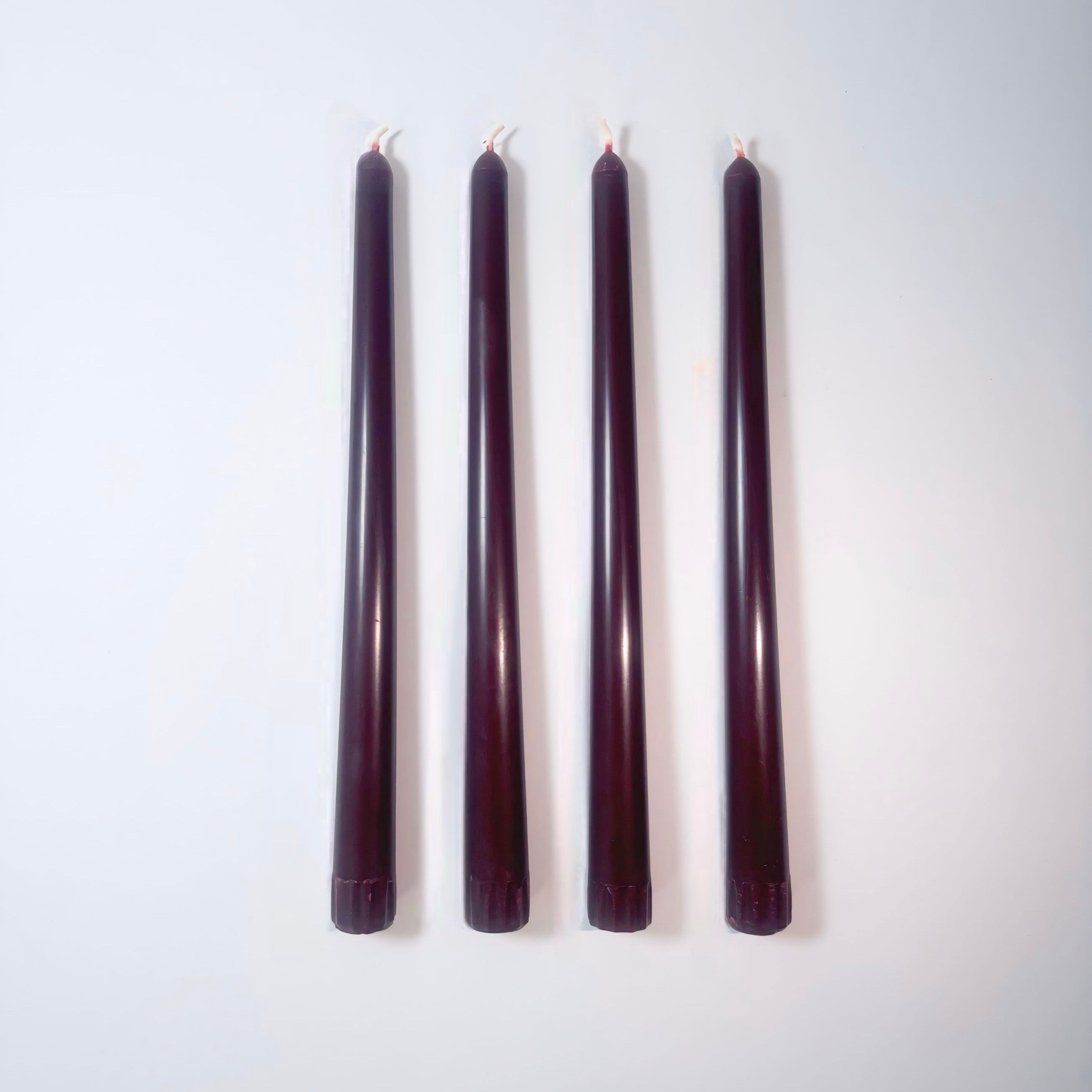 Five dark purple candles of varying lengths on a white background