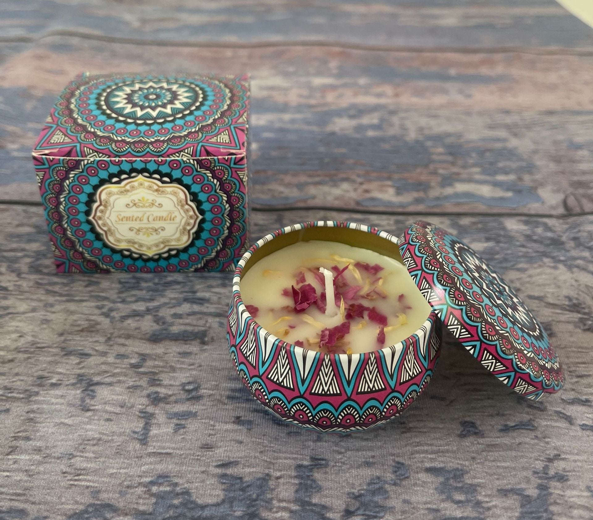 Decorative candle in a tin with a colorful lid on a wooden surface