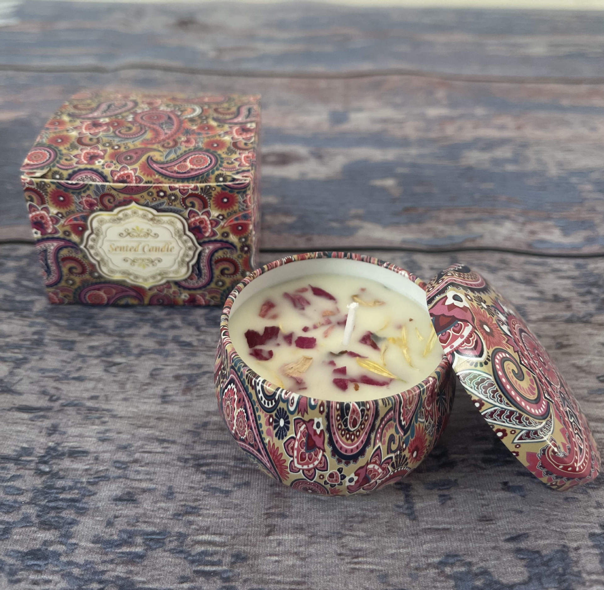 Decorative candle in a paisley-patterned holder with matching box on a wooden surface