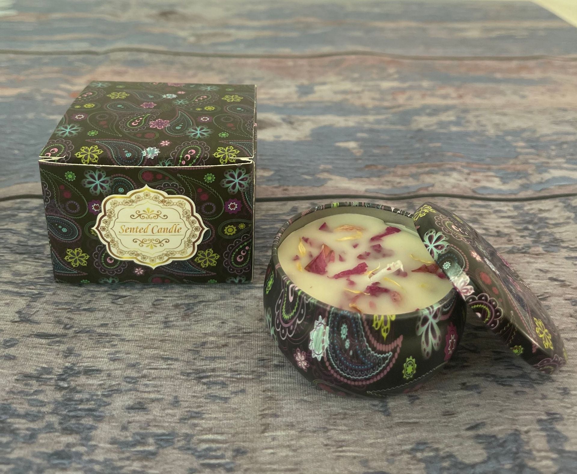 Decorative candle in a black box with floral patterns on a wooden surface