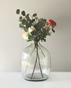 Clear glass vase with greenery and flowers on a white surface and background