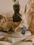 Earrings with blue and gold details on a textured surface with a vase in the background